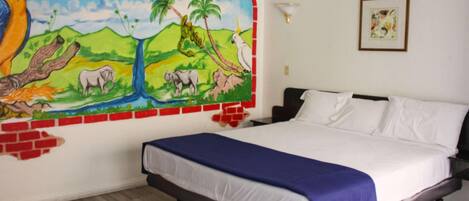 A bedroom with a bed, a mural on the wall, and a framed picture.