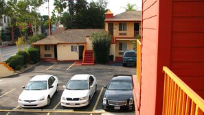 A parking lot with three cars parked in front of a building with a red exterior and a balcony. - Motel 6 Glendale, CA – Pasadena Burbank Los Angeles (Glendale)