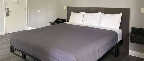 Quarto de hotel moderno com uma cama grande, uma mesa de cabeceira e chão de madeira escura.
