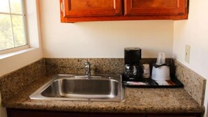 Una cucina con lavello in acciaio inossidabile, piano di lavoro in granito, mobili in legno e una macchina per il caffè.
