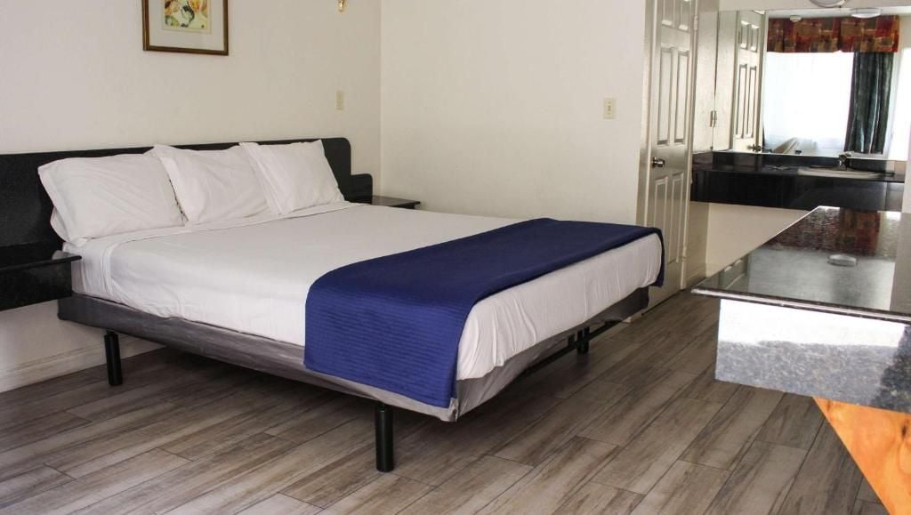 A single bed with a white mattress and a blue blanket, a black headboard, and a wooden floor.