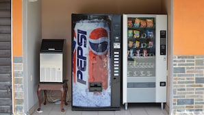 En automat med Pepsi-logo, et lille bord og et køleskab.