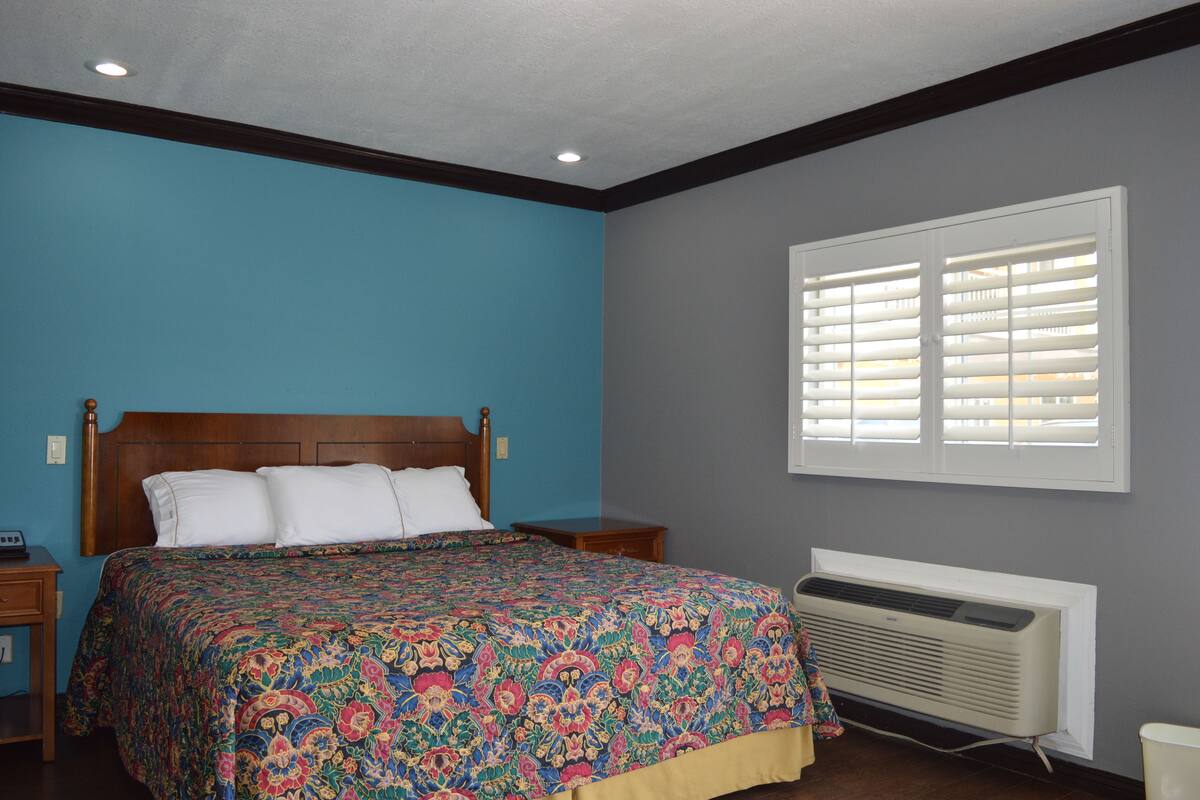 A bedroom with a bed, a window with blinds, a heater, and a nightstand.