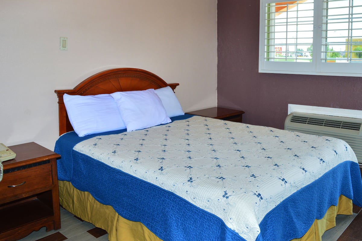 A neatly made bed with a floral patterned bedspread, a wooden headboard, and a bedside table with a lamp.