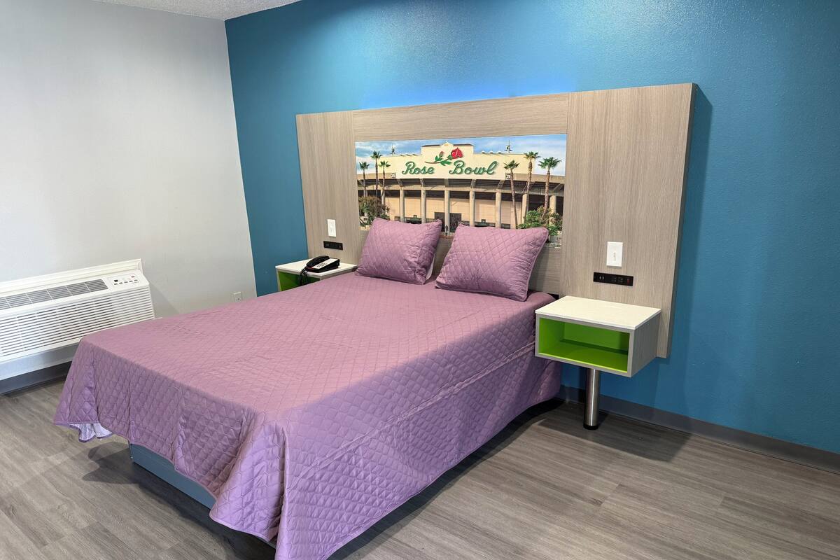 A bedroom with a bed, nightstands, a heater, and a wall-mounted sign reading "Rose Bowl".