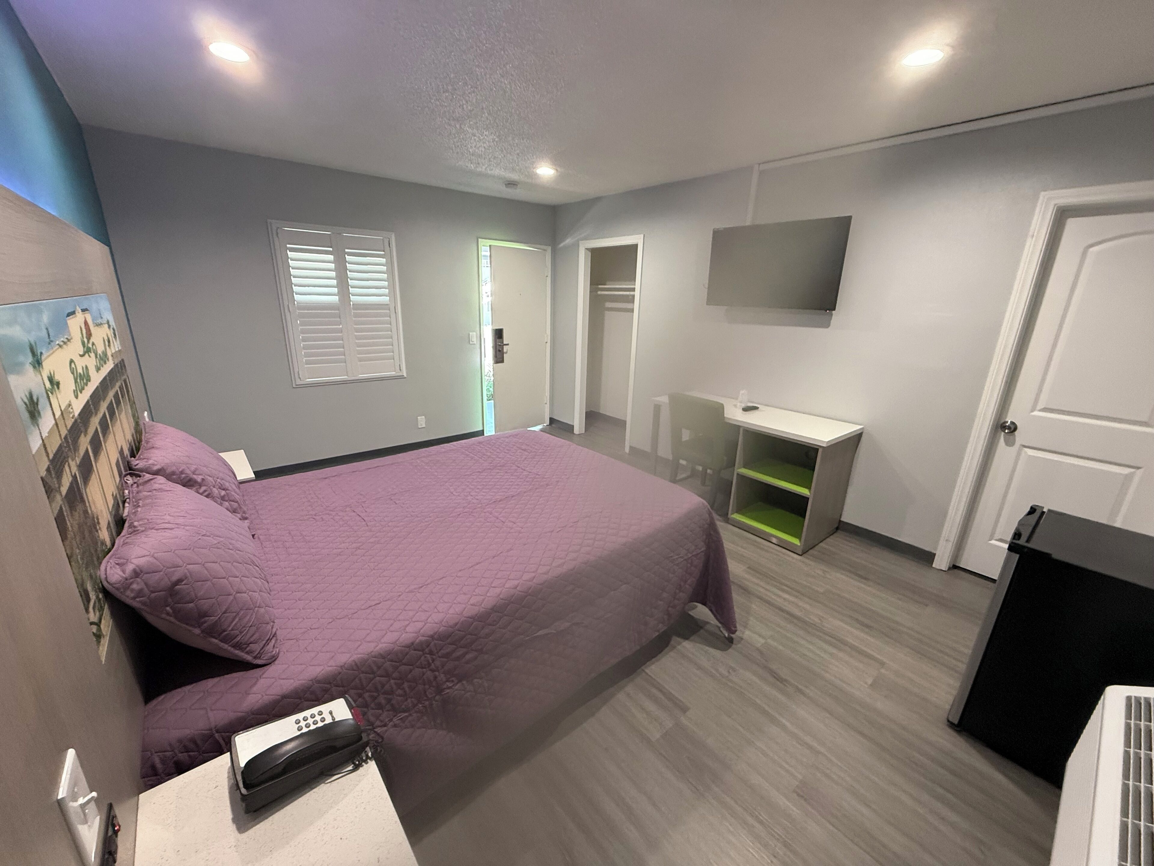 A bedroom with a bed, a desk, a chair, a TV, and a door.