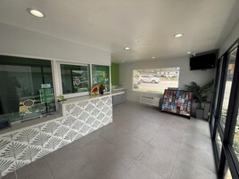 Un área de recepción con mostrador, una ventana con vista al estacionamiento y un tablón de anuncios con folletos.