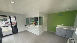 A reception area with a counter, a clock, and a view of parked cars outside. - Hi-Way Host Motel (Pasadena)