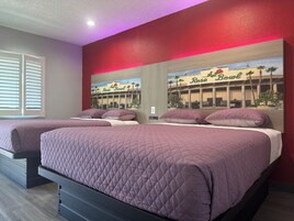 Habitación de hotel con dos camas, un ventanal con persianas y un mural de un edificio con palmeras.