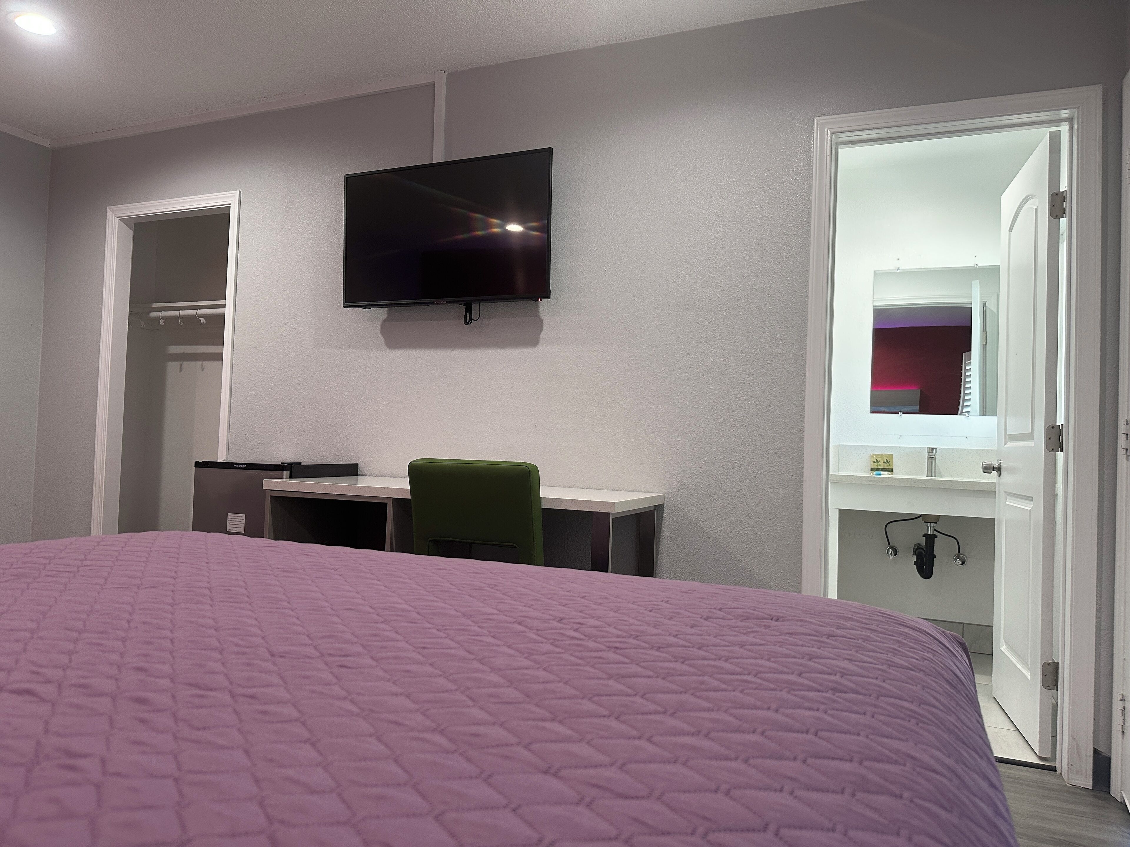 Quarto com cama, escrivaninha, cadeira, televisão e banheiro.
