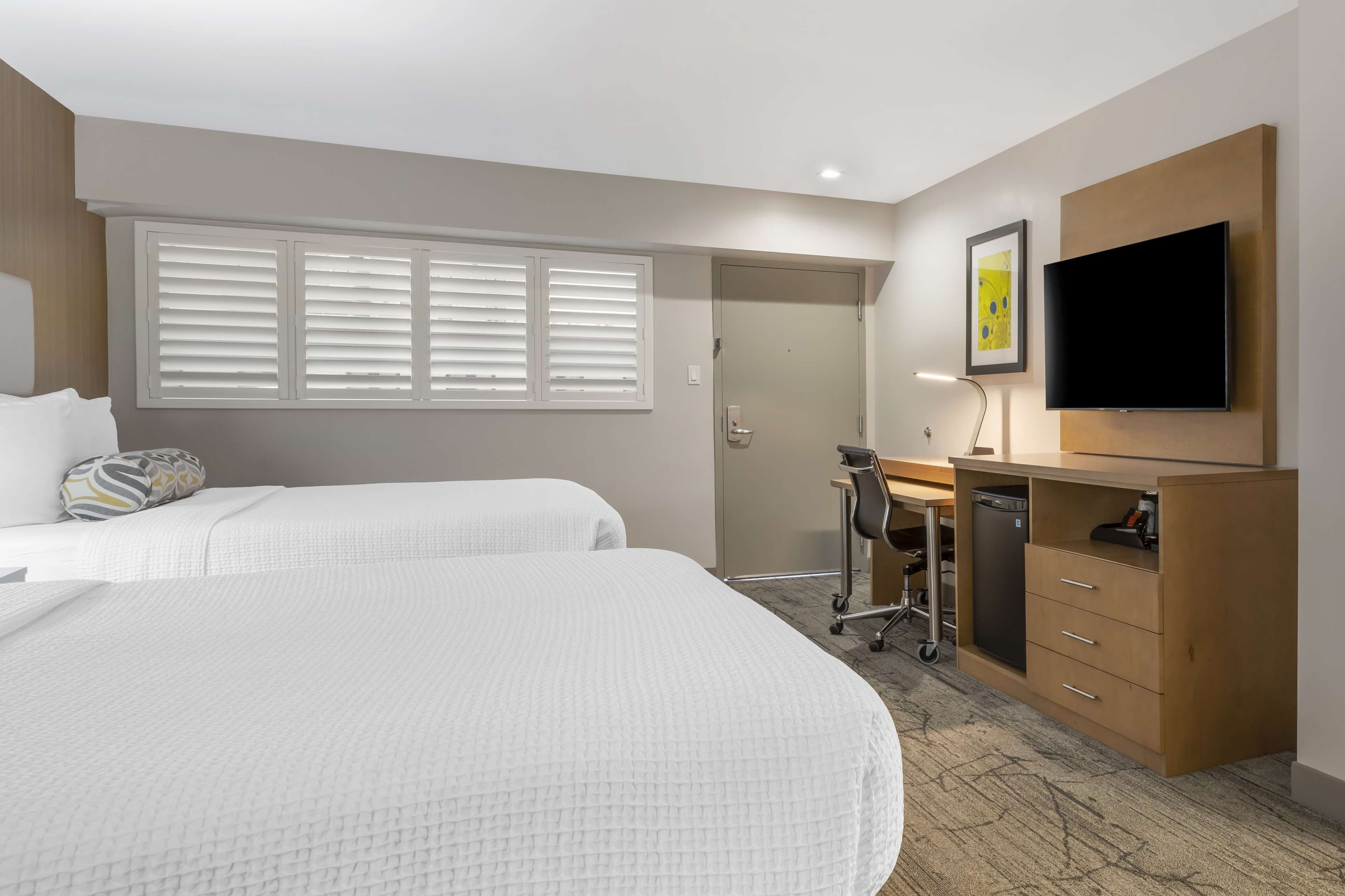 A hotel room with two beds, a desk, a chair, a television, and a door leading to a bathroom.
