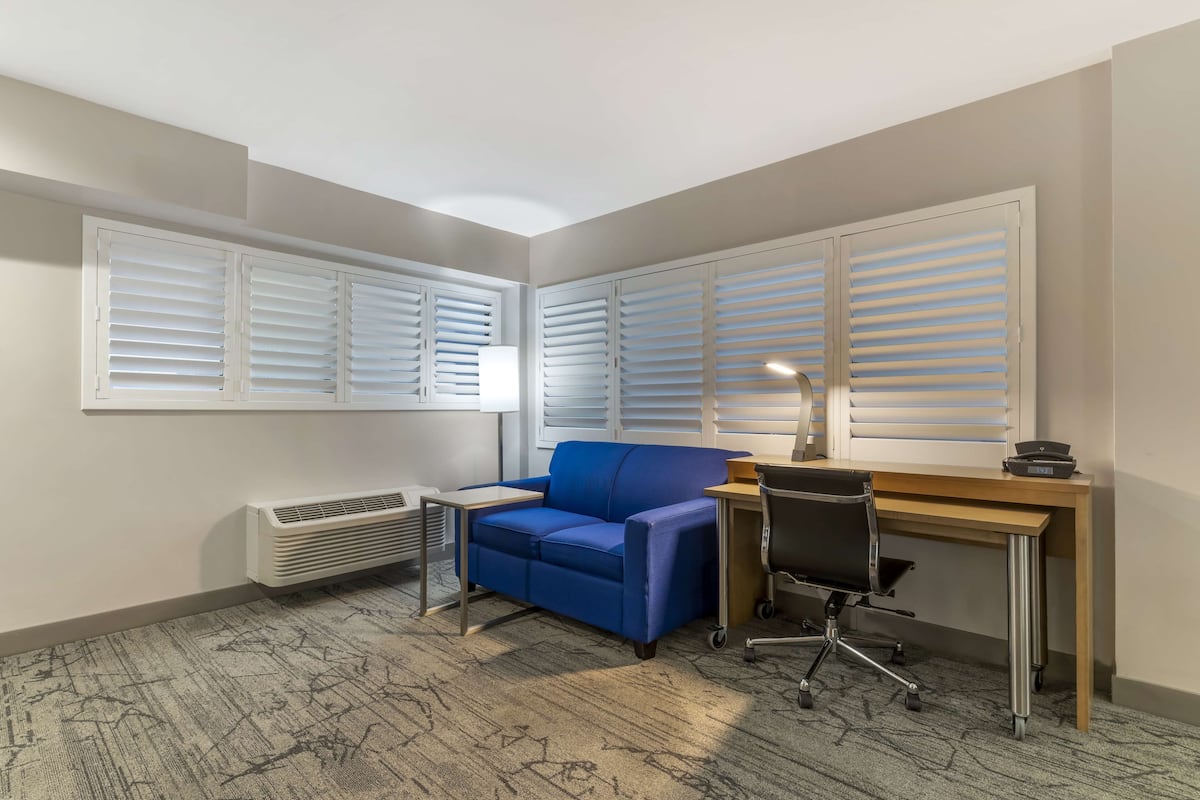 Une pièce d’angle avec un canapé bleu, un bureau, une chaise et un radiateur.