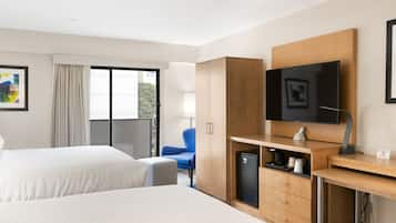 A hotel room with two beds, a desk with a television, a chair, and a minibar.