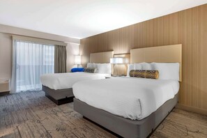 Une chambre d’hôtel avec deux lits, une grande fenêtre avec des rideaux légers, un mur en bois et un sol recouvert de moquette.