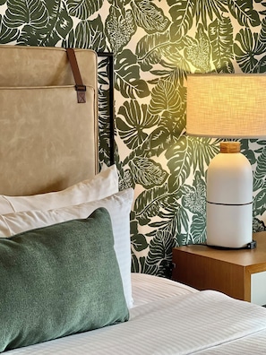 A bed with white and green pillows, a nightstand with a lamp, and a wall with a leafy pattern.