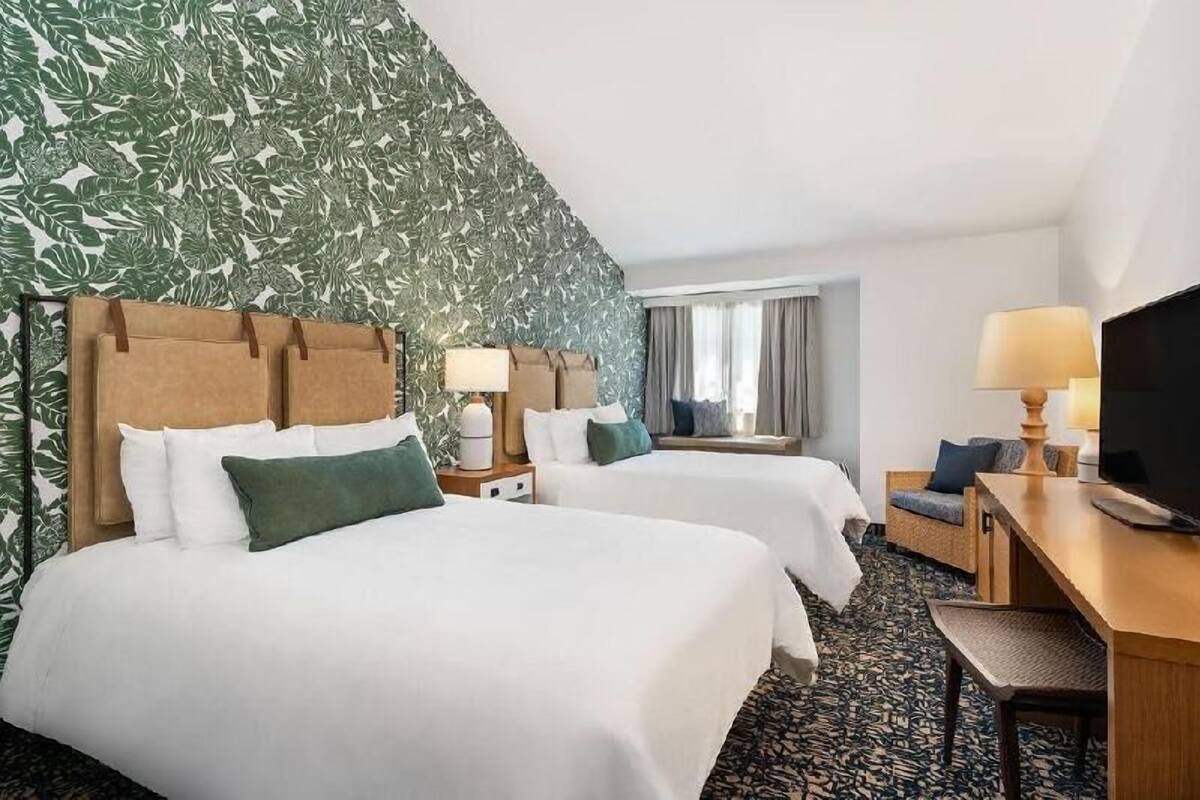 A hotel room with two beds, a desk, a TV, and a window with curtains.