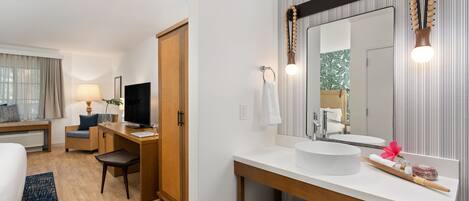 A hotel room with a bed, a desk, a chair, a TV, a large mirror, a sink, and a window with curtains.