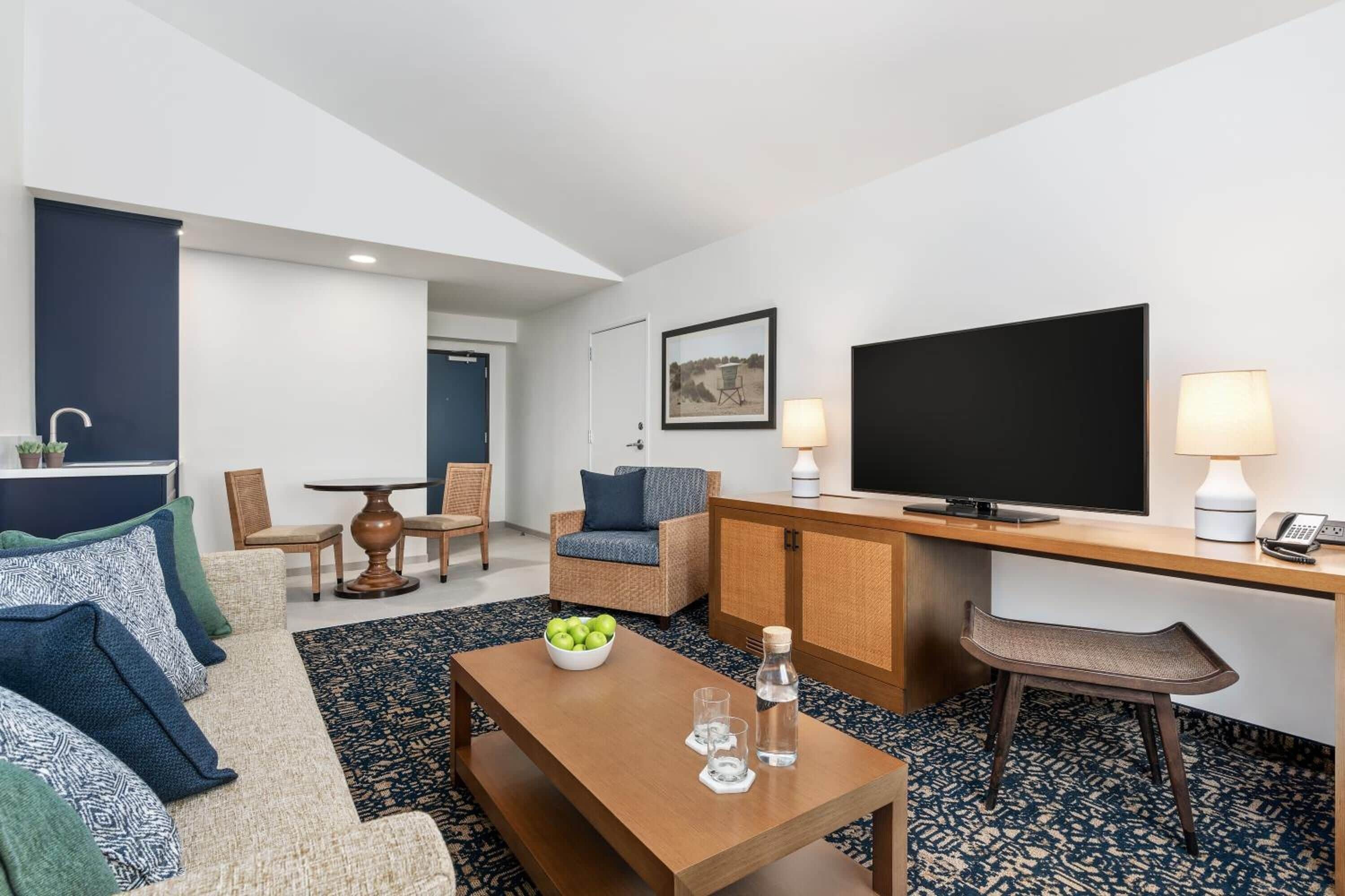 Ein modernes Hotelzimmer mit Sofa, Sessel, Esstisch und Fernseher.