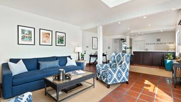 Uma sala de estar moderna com um sofá azul, poltrona estampada e uma mesa de centro. Uma área de cozinha é visível ao fundo, com uma placa que diz "Mason Beach Inn".