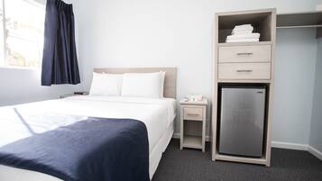 Una habitación de hotel con cama, mesita de noche, minibar y armario.