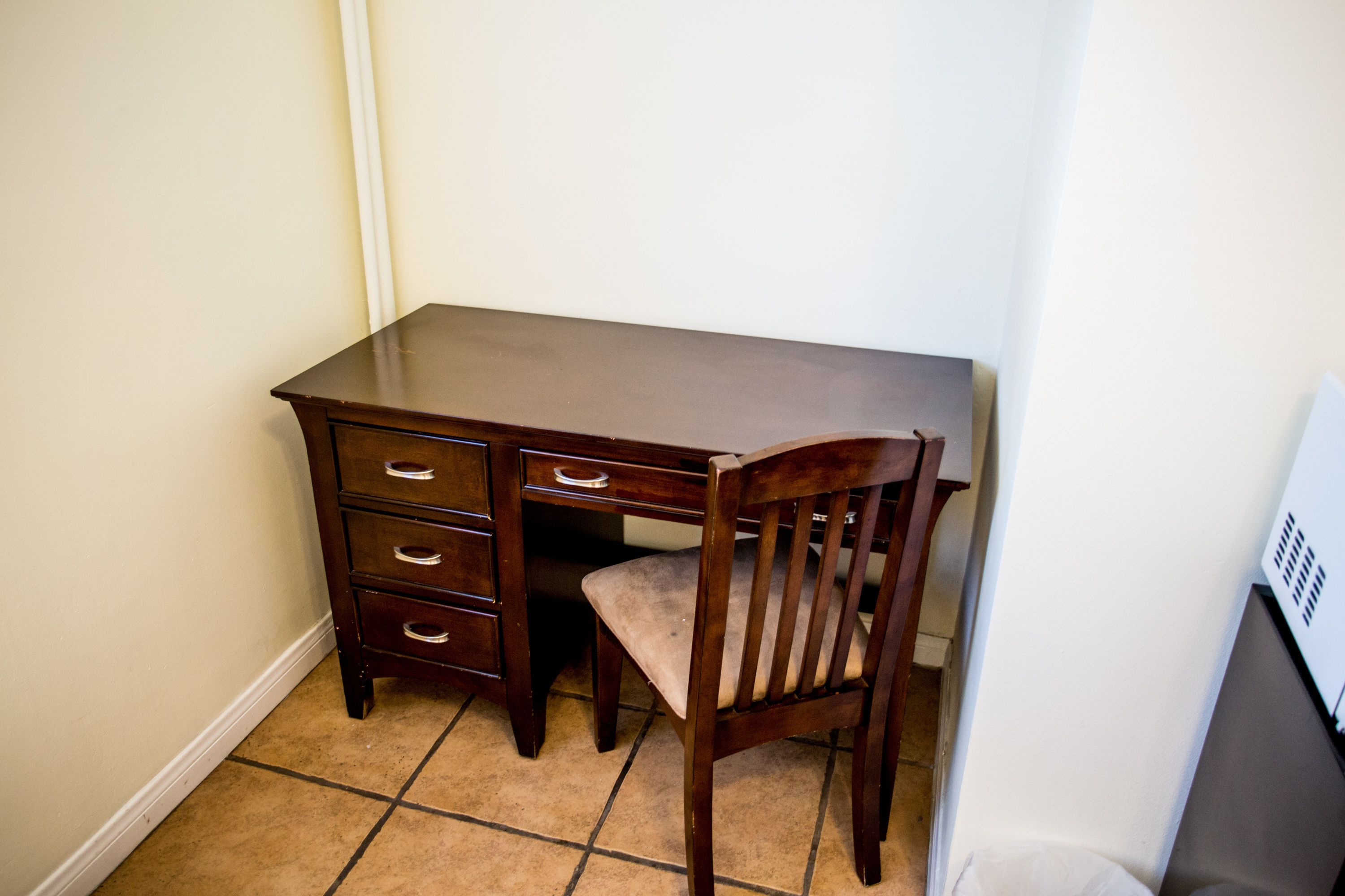 A corner room with a wooden desk, a chair, and a tiled floor.