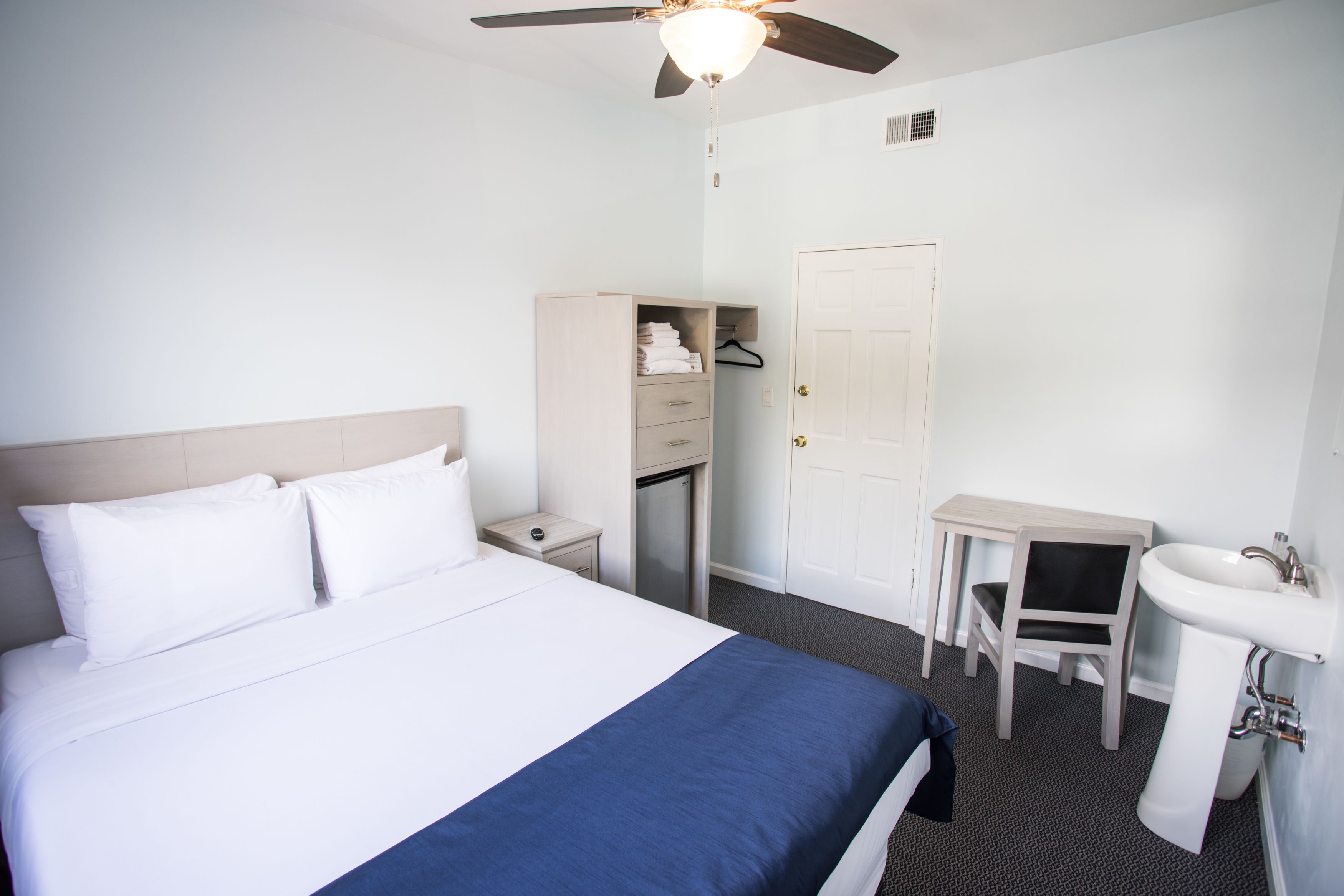 A hotel room with a bed, a desk, a chair, a sink, and a wardrobe.