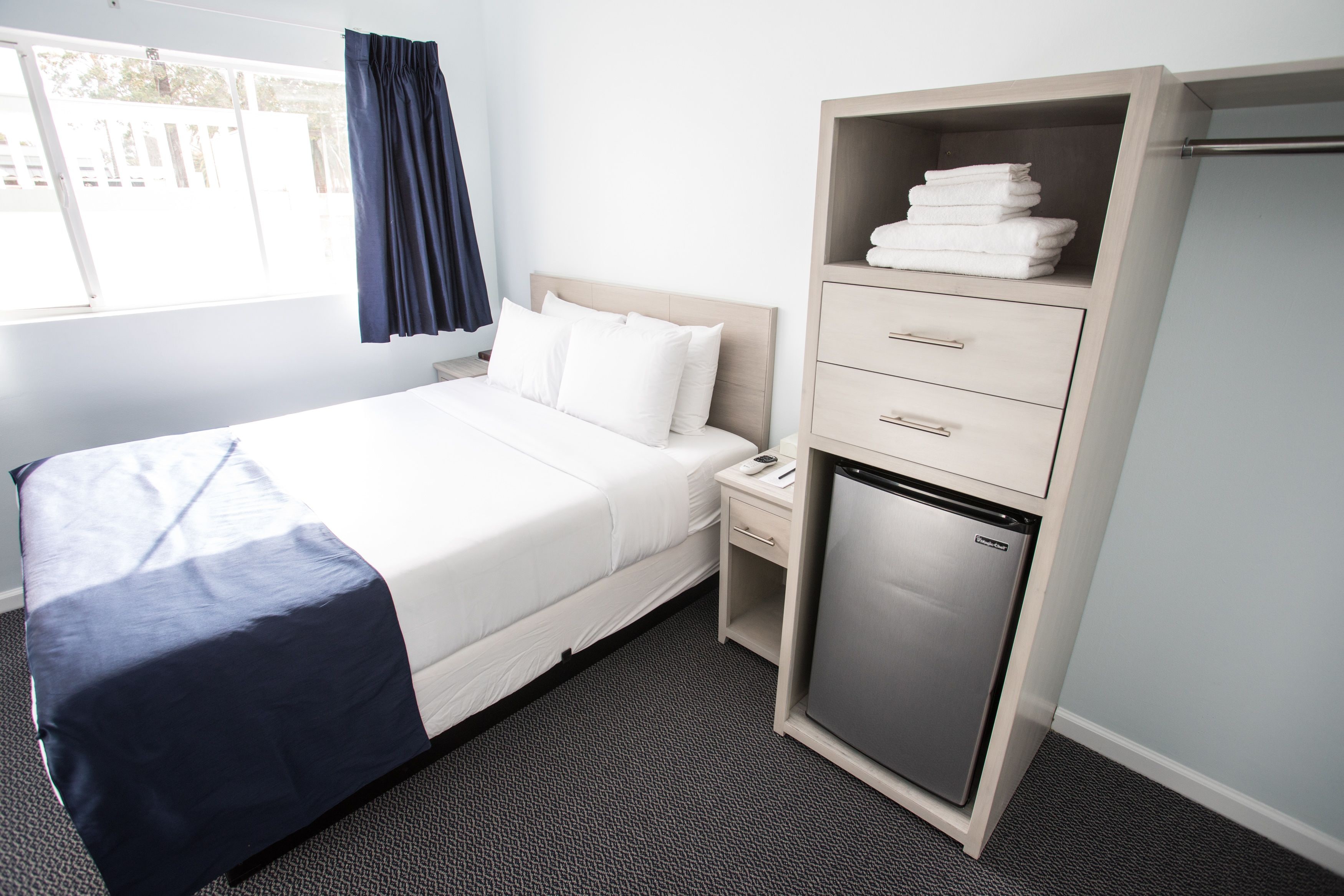 A hotel room with a bed, a nightstand, a mini-fridge, and a wardrobe.