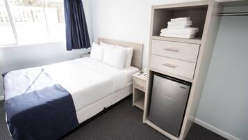 A hotel room with a bed, a nightstand, a mini-fridge, and a wardrobe.