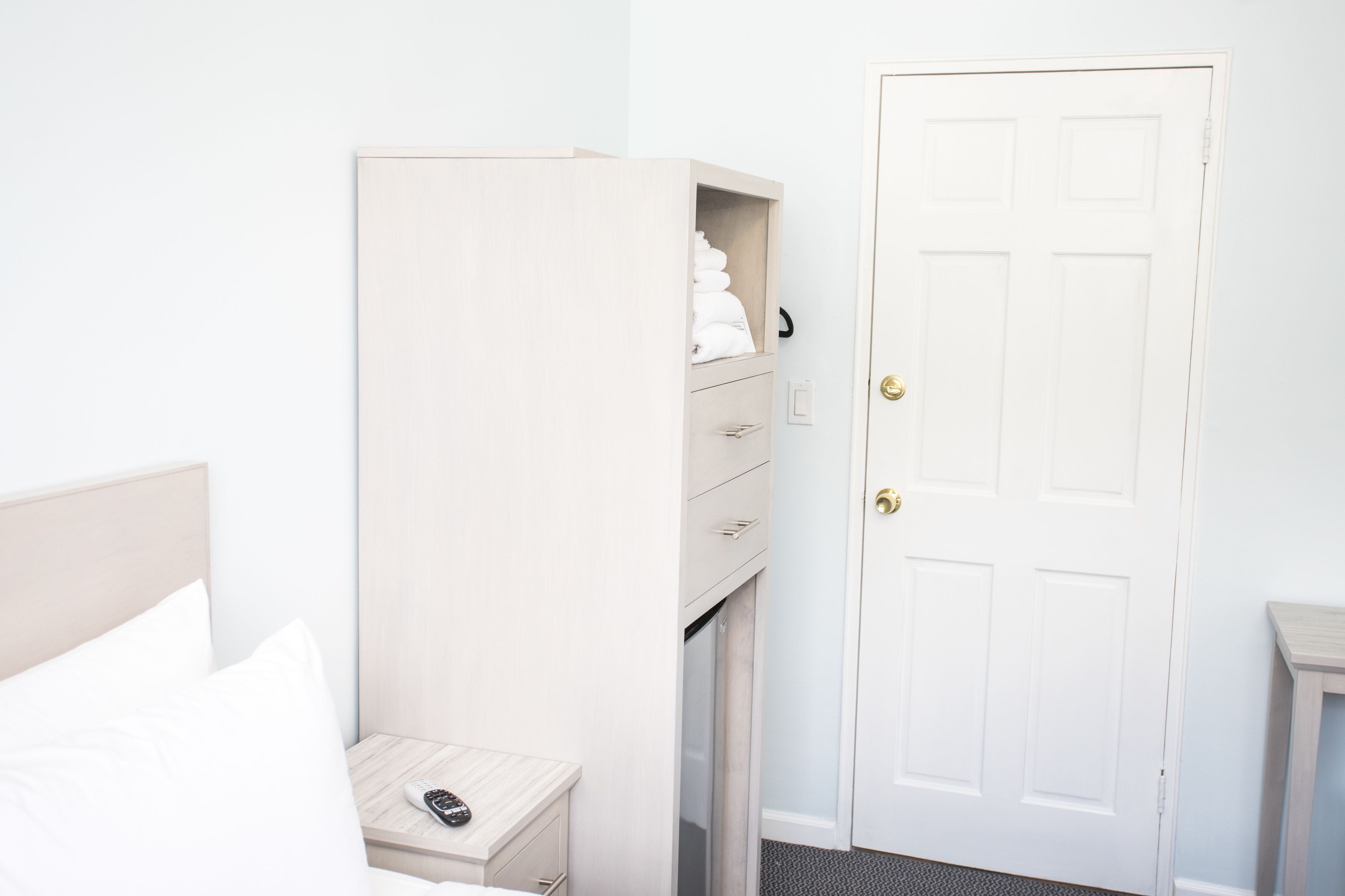 A hotel room with a bed, a bedside table with a remote control, a wardrobe, and a door.