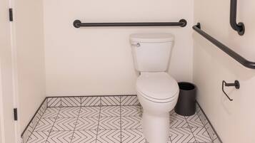 A small, modern bathroom with a white toilet, black grab bars, and a geometric patterned floor.
