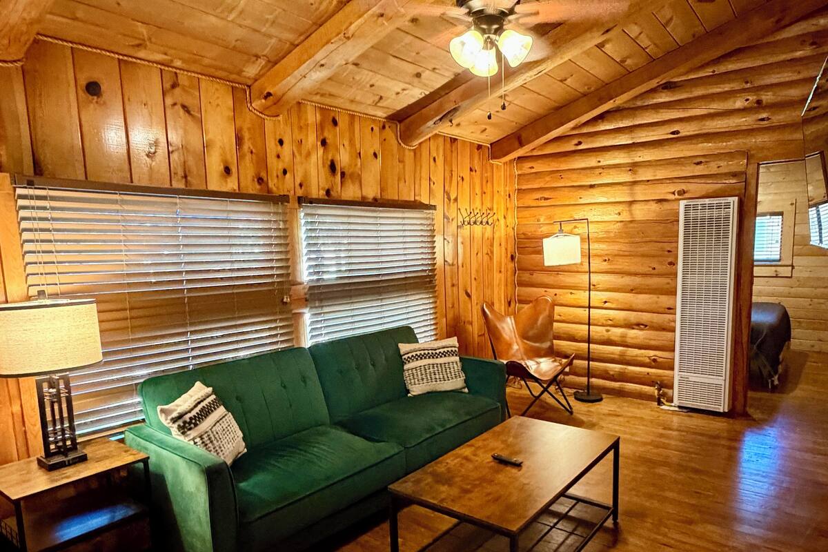 A log cabin interior with a green sofa, a small table, a ceiling fan, and wooden walls.