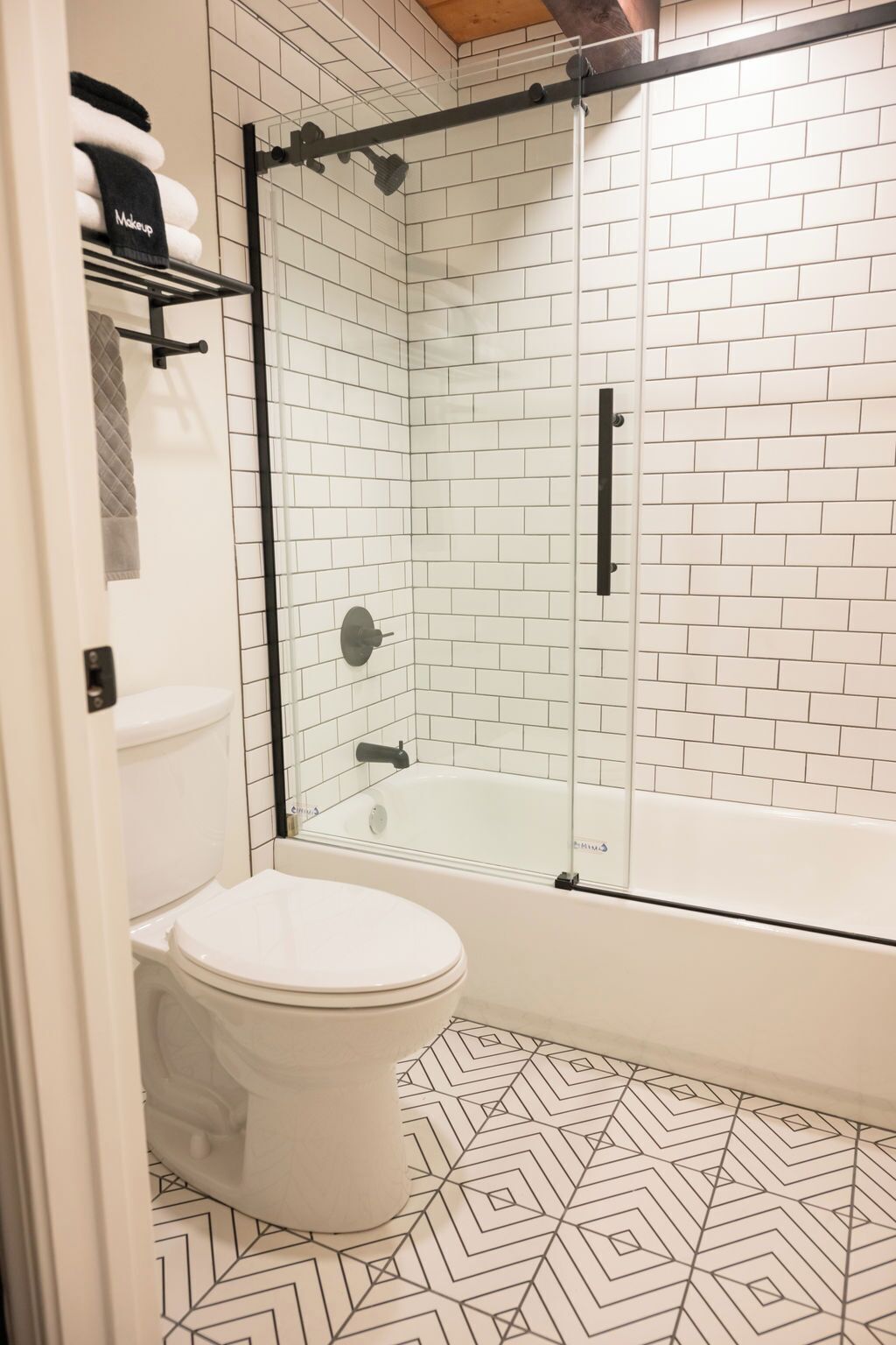 Een badkamer met een wit toilet, een douche met glazen wanden en een vloer met een patroon.