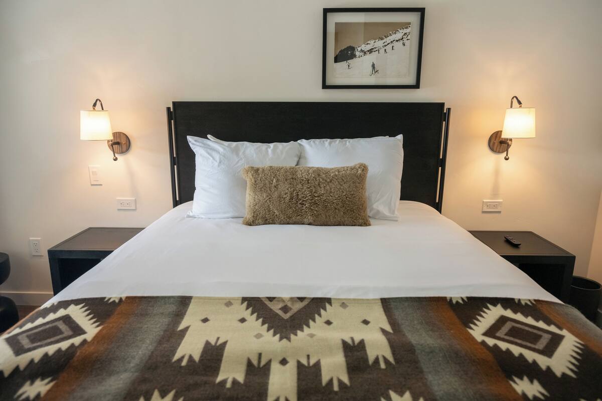 A neatly made bed with a patterned blanket, two bedside lamps, and a framed picture on the wall.