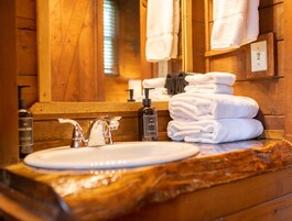 Un baño de madera con un lavamanos, un espejo y una pila de toallas blancas.