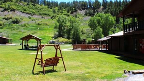 Una cabaña con un columpio, mesas de picnic y vistas a una ladera boscosa.
