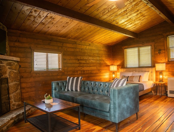 A cozy cabin interior with a wooden ceiling, a sofa, a bed, and a fireplace. - High Creek Lodge & Cabins (Pagosa Springs)