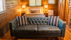 Un dormitorio tipo cabaña de madera con una cama grande, dos lámparas de noche y un sofá de cuero.