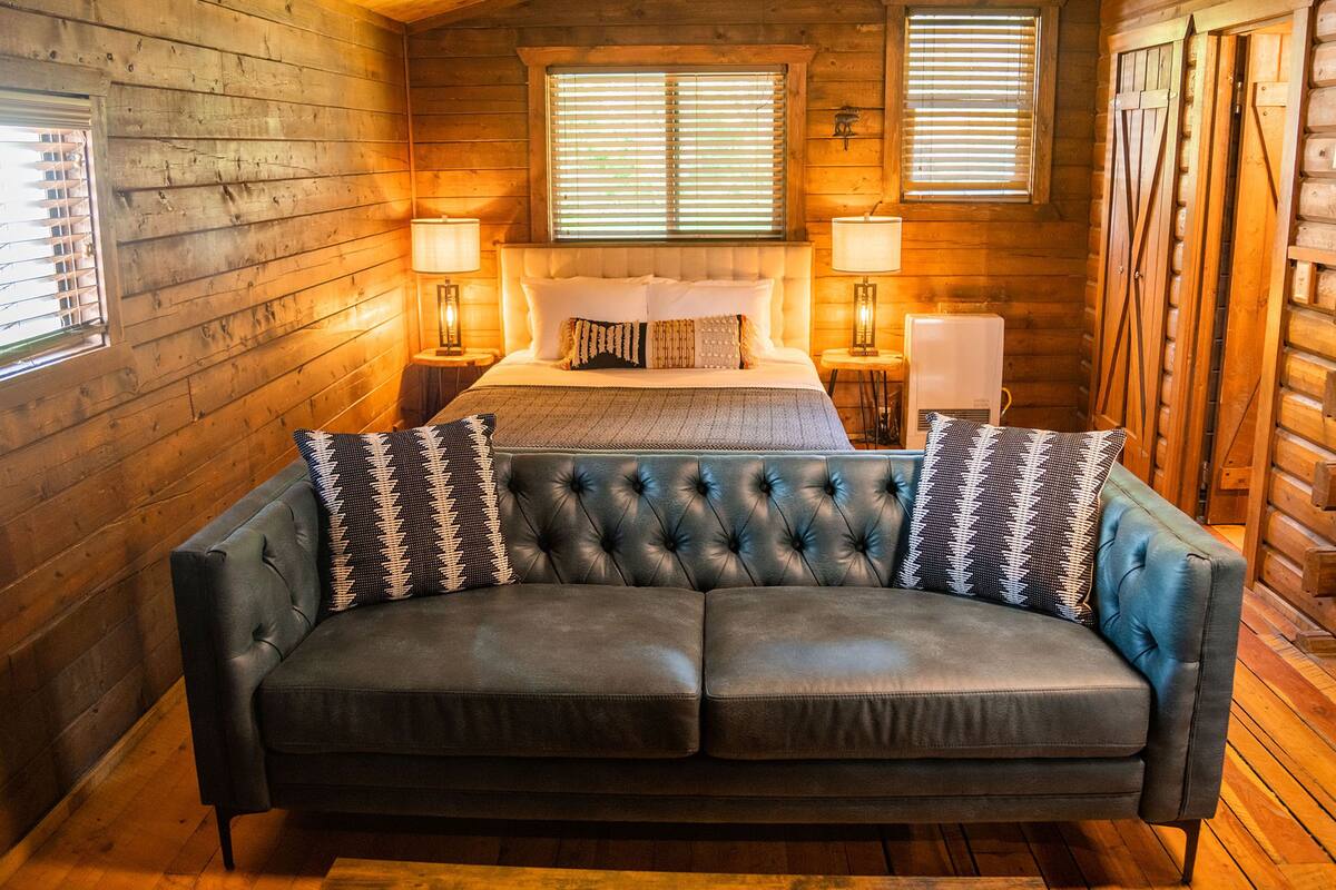 A log cabin bedroom with a large bed, two bedside lamps, and a leather sofa.