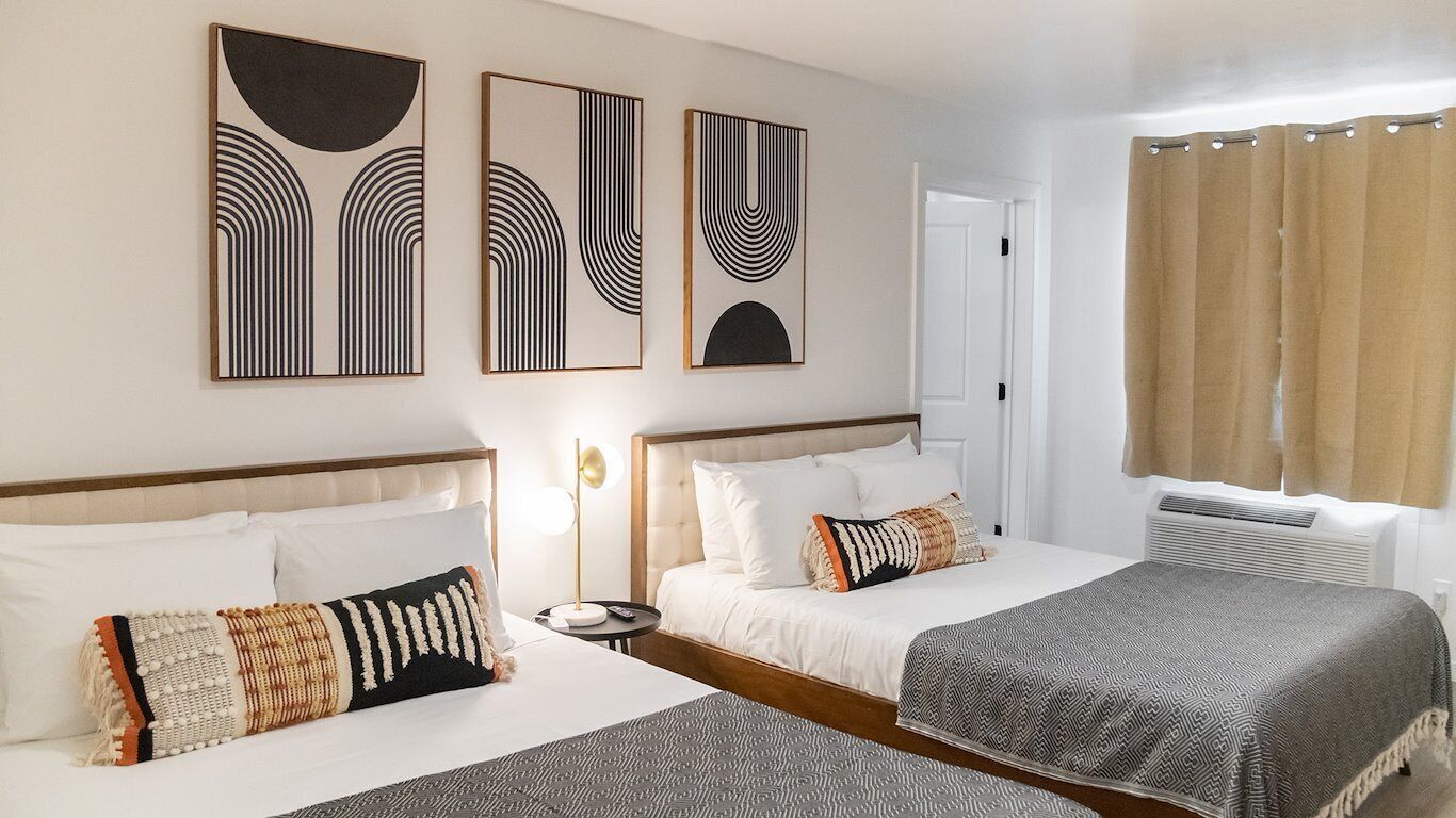 A hotel room with two beds, a bedside table with a lamp, and artwork on the wall.