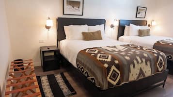 Habitación de hotel con dos camas, cada una con un edredón estampado, lámparas de noche, una mesita pequeña y un banco de madera.