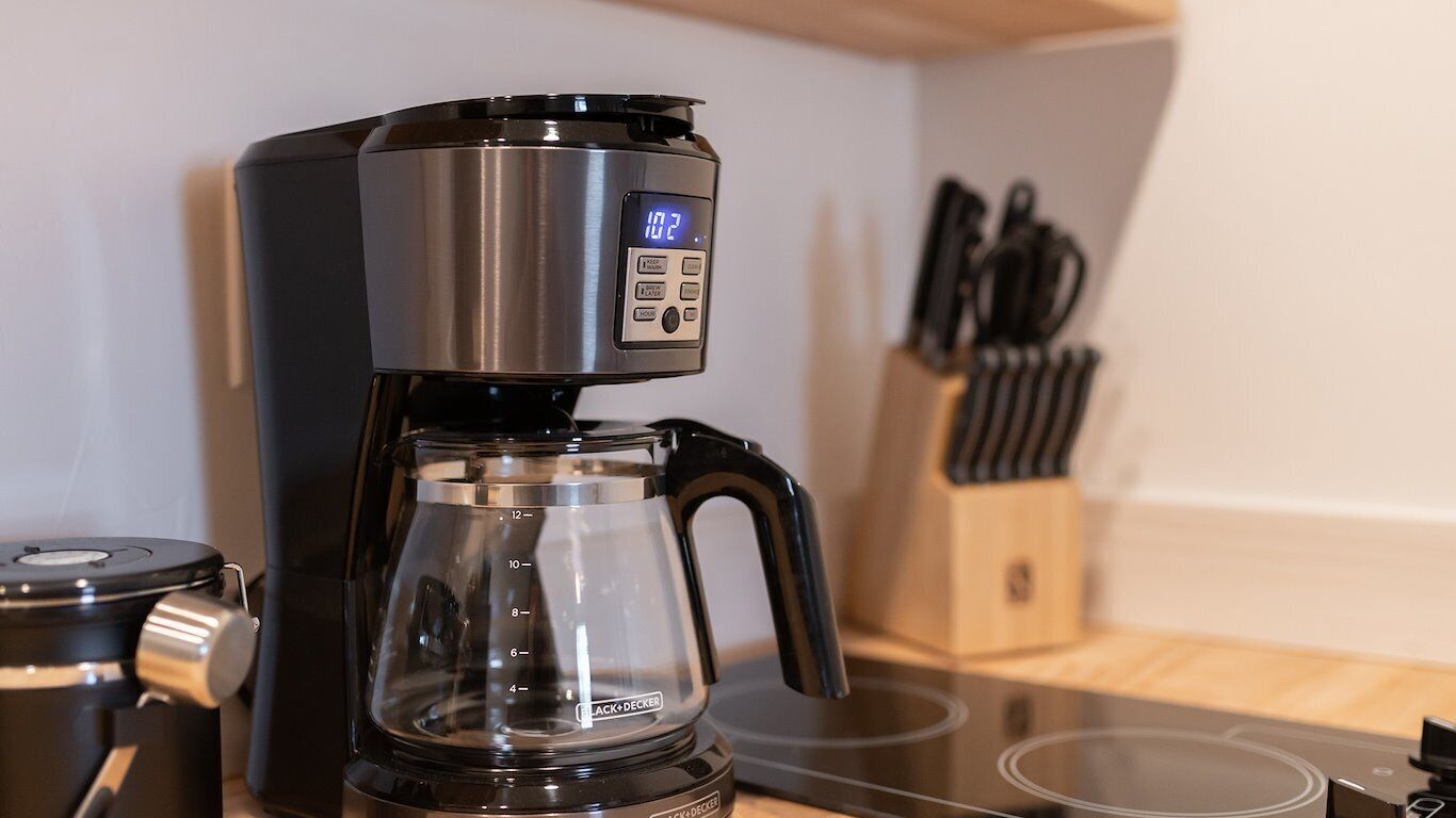 Una cafetera con pantalla digital, una jarra de vidrio y un bloque de cuchillos al fondo.