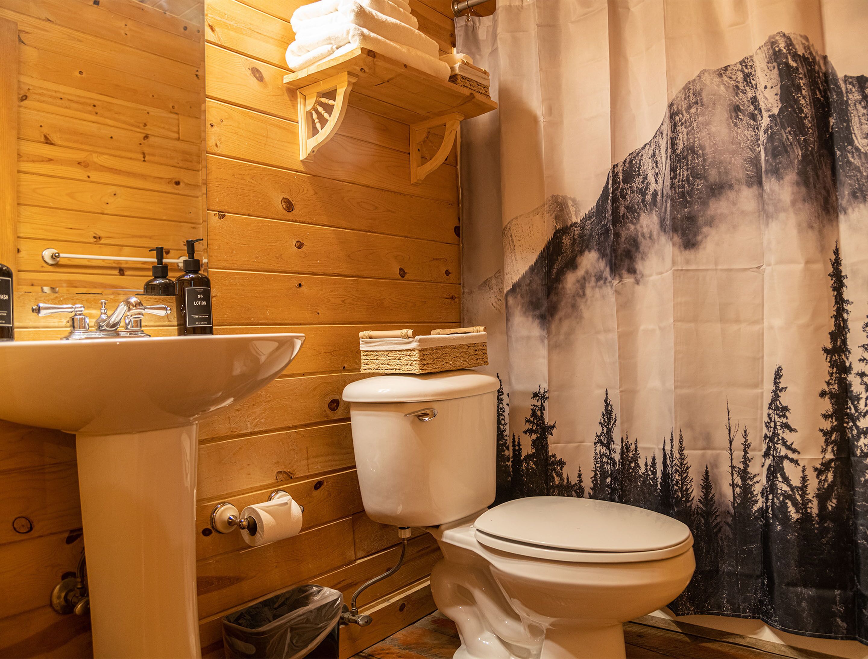 A wooden bathroom with a sink, toilet, and a shower curtain depicting a mountain scene.