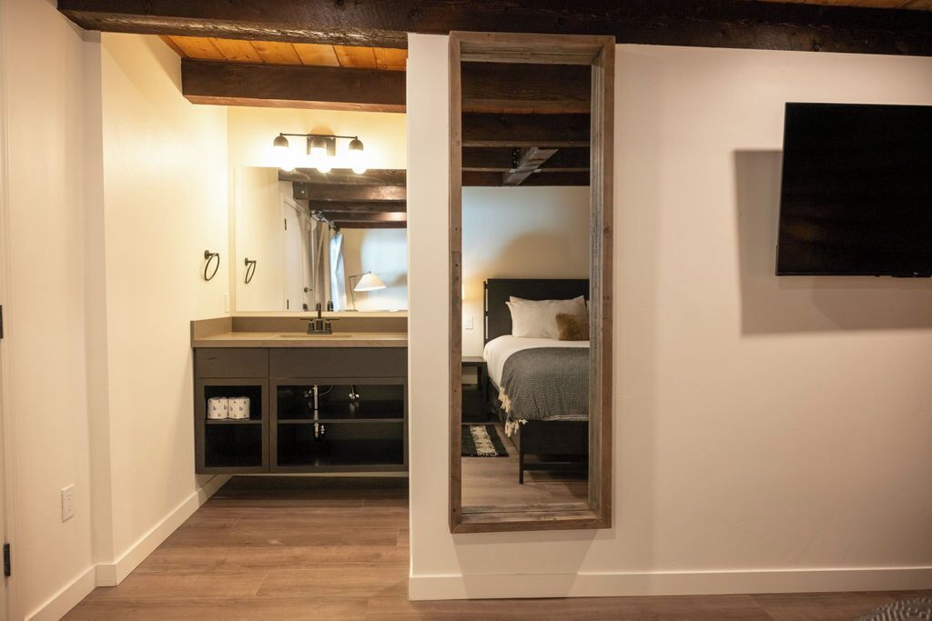 A bedroom with a bed, a nightstand, a mirror, and a wall-mounted TV.