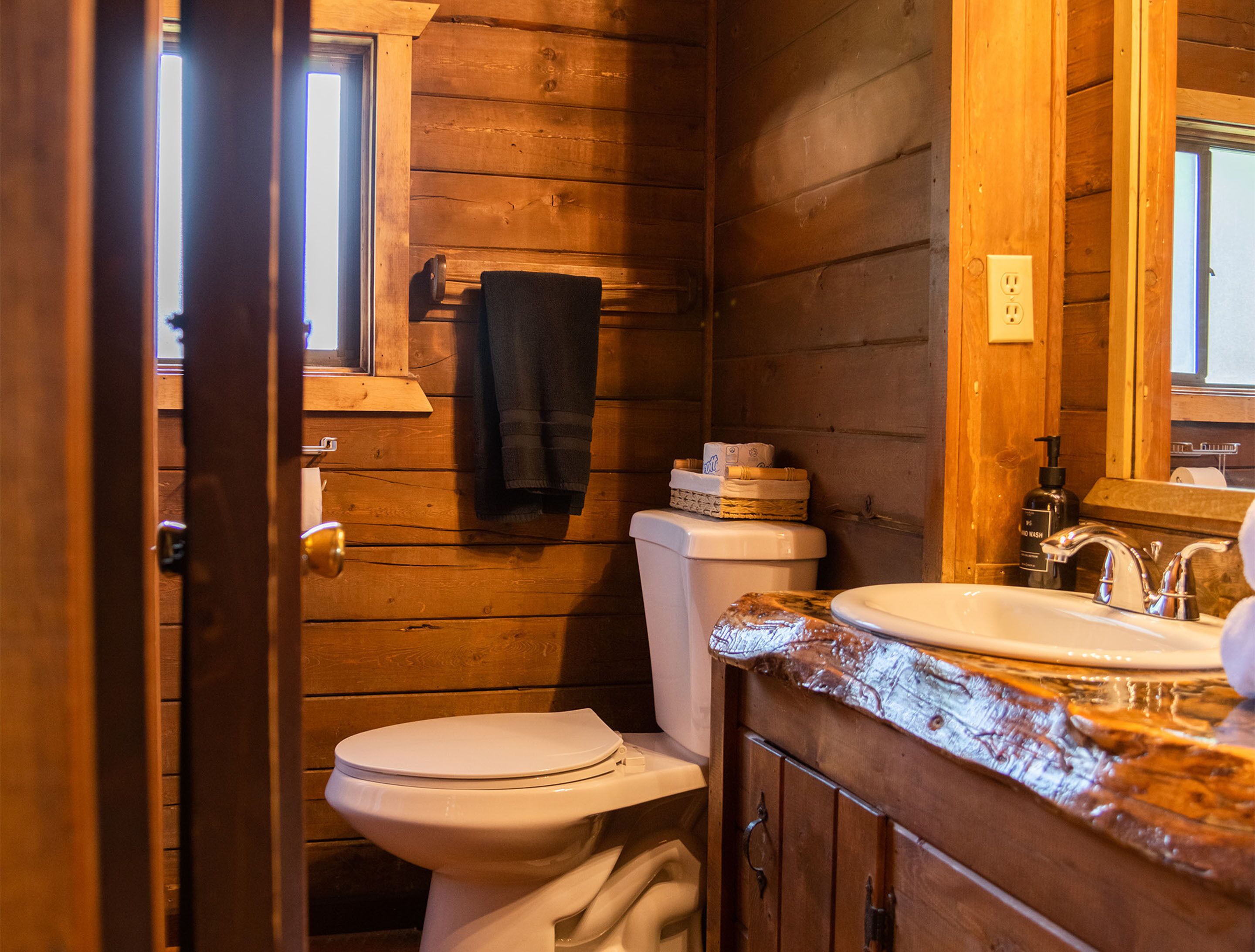 Une salle de bain rustique, aménagée dans une cabane en bois, avec des toilettes, un lavabo et une serviette accrochée au mur.