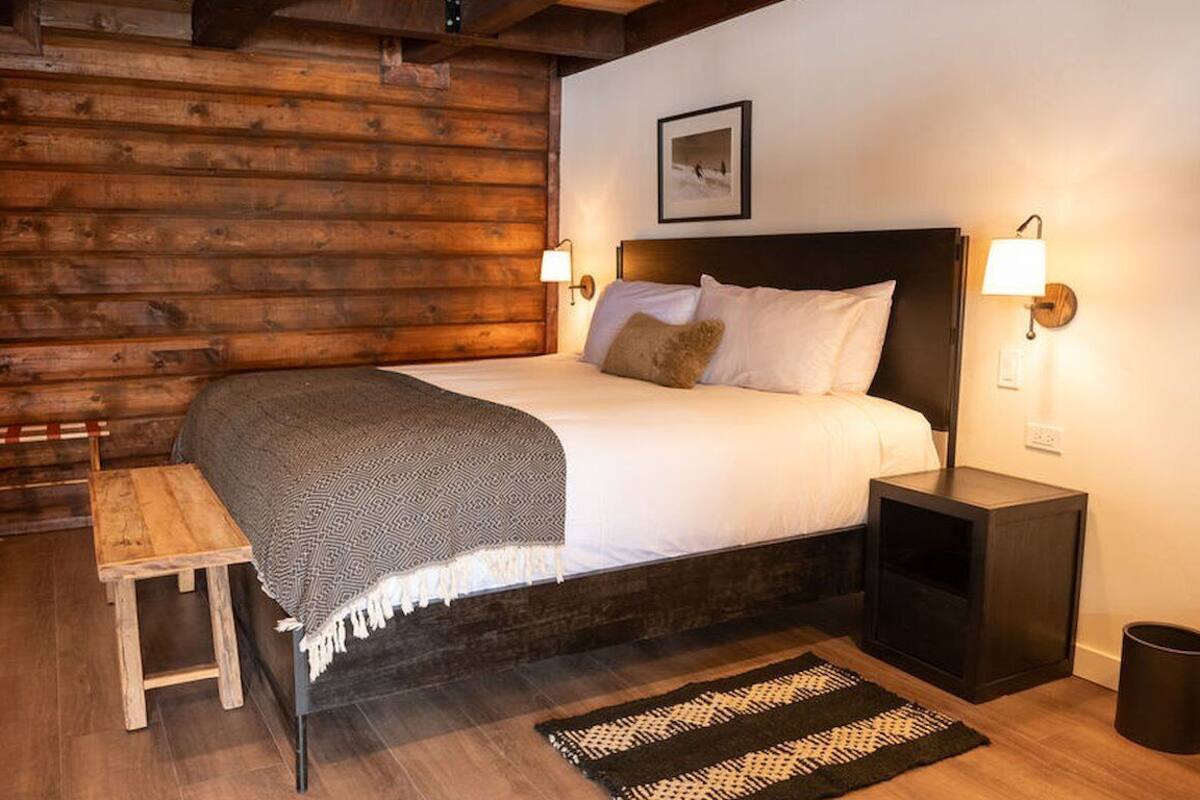 A wooden log cabin-style bedroom with a bed, bedside tables, and a bench.