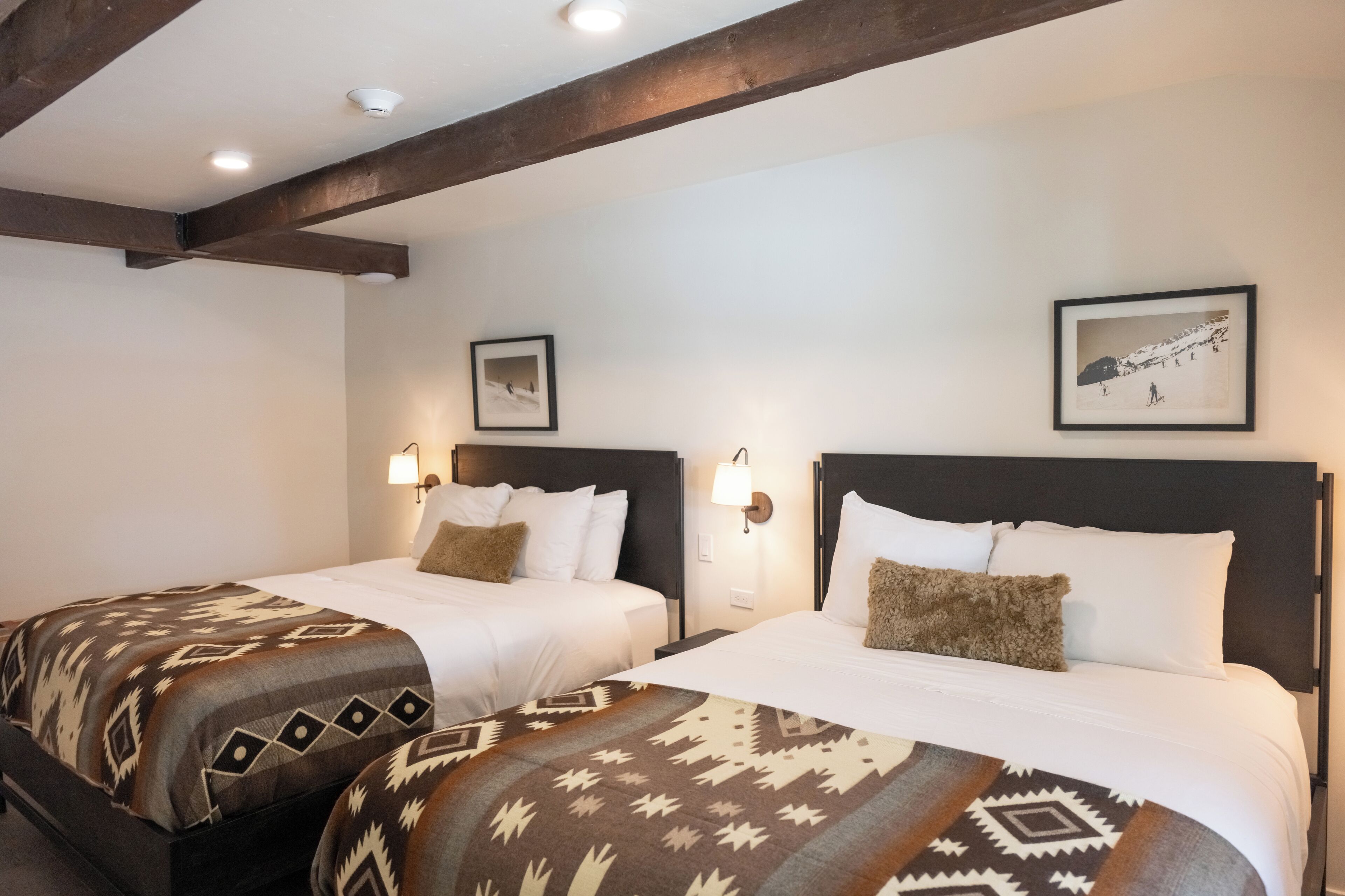 Hotelkamer met twee bedden, elk voorzien van beddengoed met een patroon, een houten balk in het plafond en wandlampen.