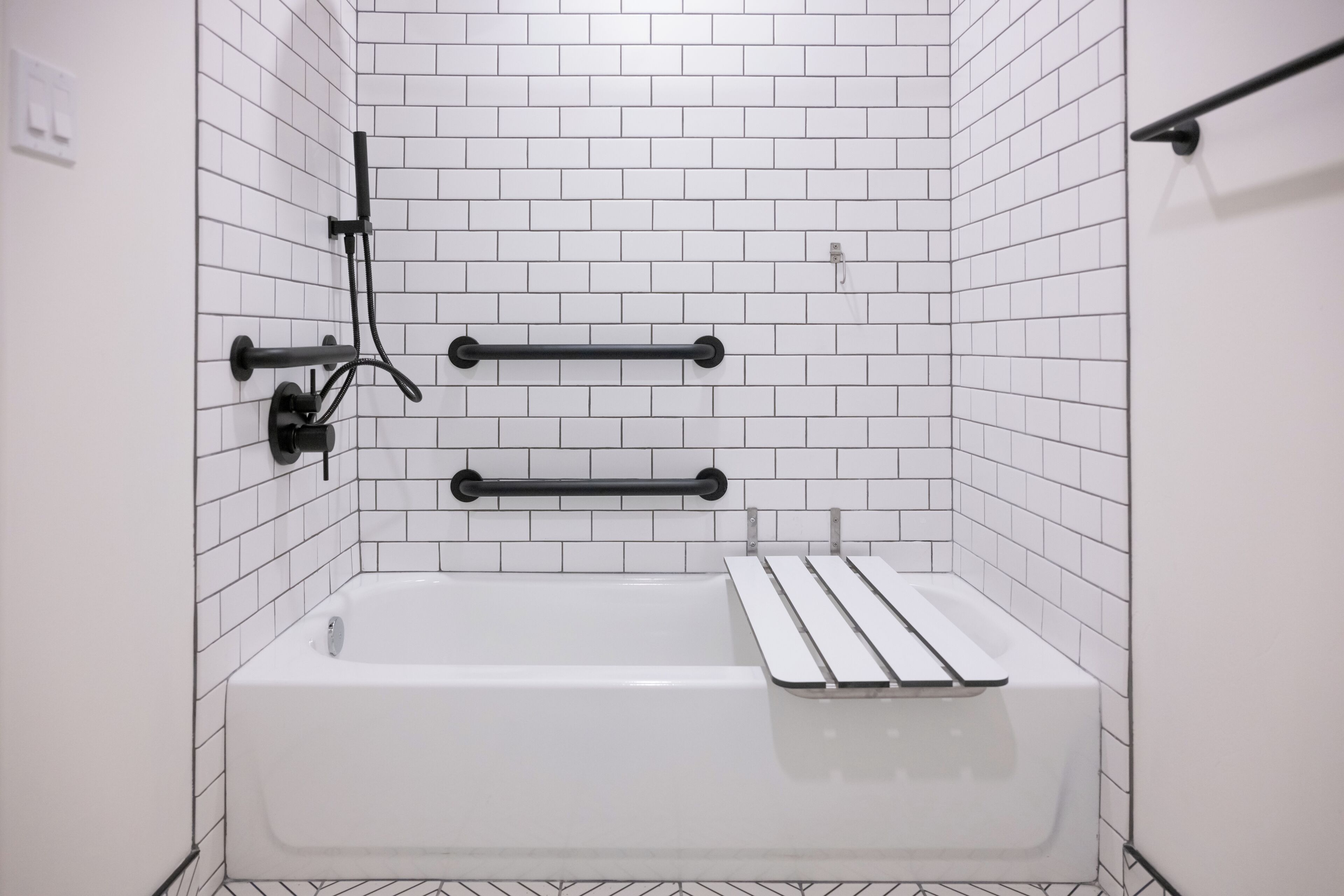 Un baño con paredes de azulejos blancos, una bañera, dos barras para toallas y un cabezal de ducha.