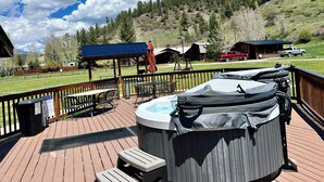 Una terraza de madera con asientos al aire libre, un jacuzzi y vistas a un paisaje montañoso.