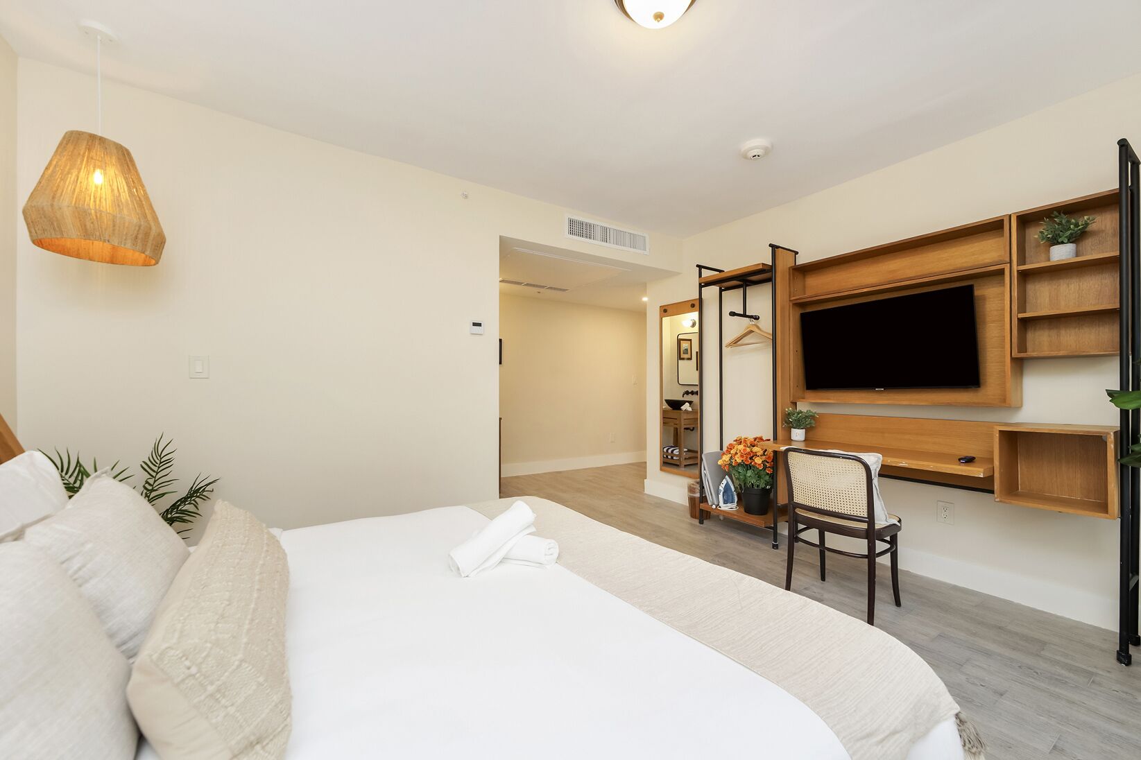 Une chambre d’hôtel avec un grand lit, un téléviseur fixé au mur, une chaise et une petite table agrémentée d’une plante.