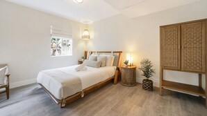 Een slaapkamer met een houten bed, een bedlamp, een klein rond tafeltje en een potplant.